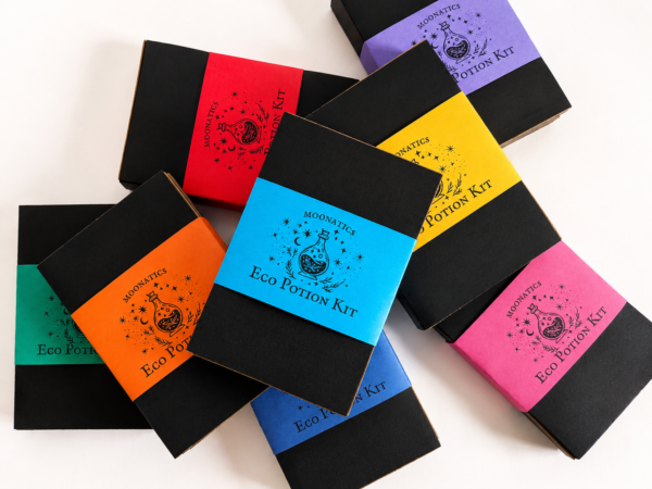 Assortment of Moonatics Eco Potion Kits with colourful paper belly bands in blue, orange, yellow, red, pink, purple and green, arranged in an overlapping flat lay on a white background.
