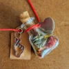 necklace_bottle_heart Handmade heart-shaped potion bottle necklace filled with colourful dried flower petals, hanging from a red cord with a heart charm and wish tag.
