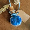 necklace_bottle_round Handmade potion bottle necklace filled with blue crystal gems. The glass bottle hangs from a blue cord and features a cork stopper, metal feather charm, tree charm and blank wish tag.