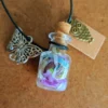 necklace_bottle_square Glass potion bottle necklace filled with colourful Pixie Paper, hanging from a dark blue cord with butterfly and owl charms, cork stopper and blank wish tag.
