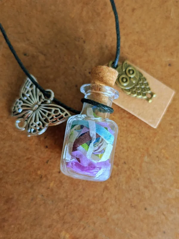 necklace_bottle_square Glass potion bottle necklace filled with colourful Pixie Paper, hanging from a dark blue cord with butterfly and owl charms, cork stopper and blank wish tag.