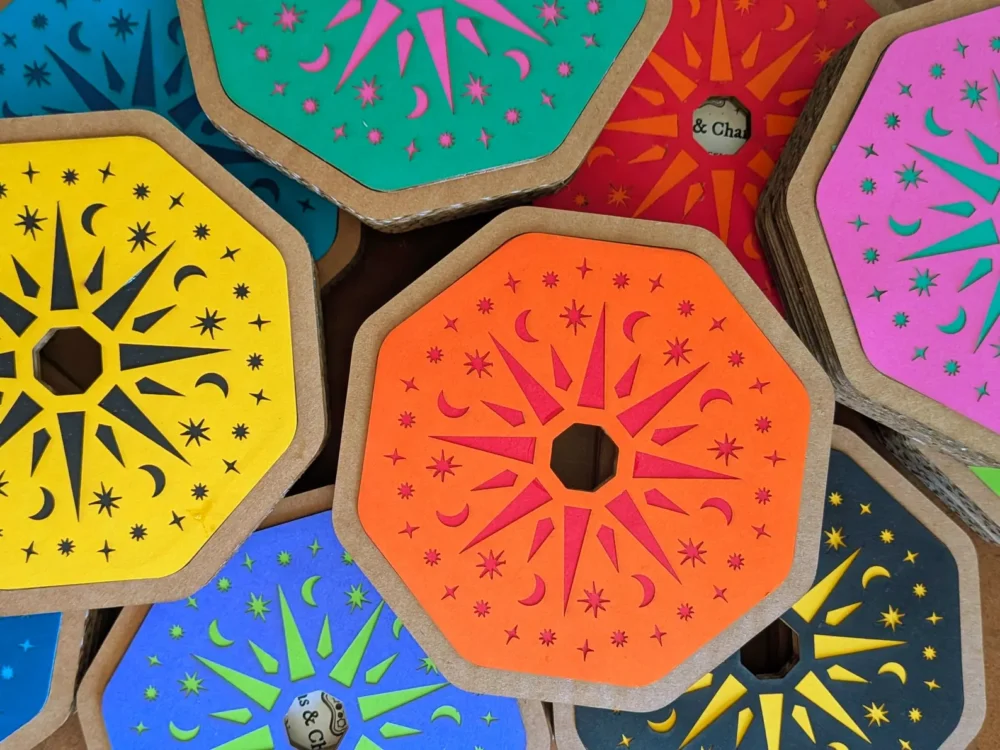 Collection of colourful Potion & Charms Necklace Kit gift boxes arranged together, showing bright laser-cut designs in blue, pink, yellow, orange and purple.