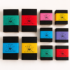 Collection of Moonatics Eco Potion Kits in black cardboard boxes with colourful paper belly bands in turquoise, red, pink, yellow, blue and purple, arranged neatly on a white background.