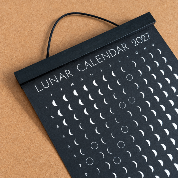 lunar-calendar-2027-black-wooden-hanger-close-up Close-up of the Moonatics 2027 lunar calendar with a black wooden hanger