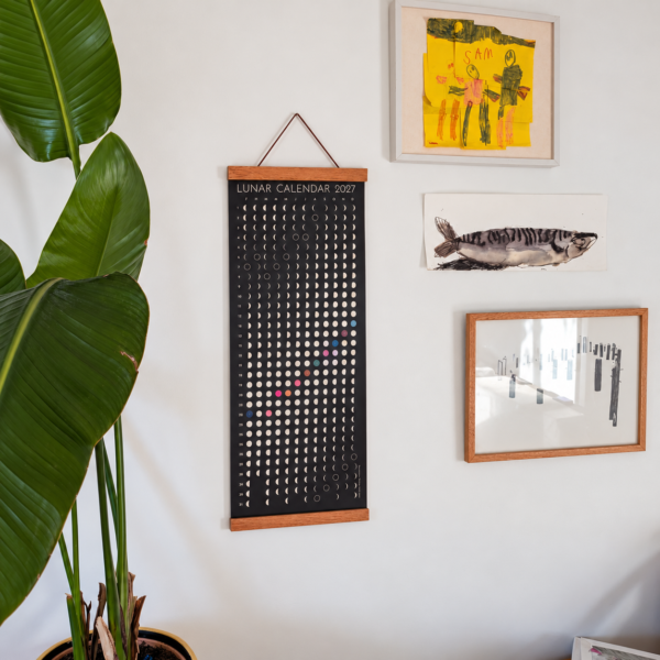 lunar-calendar-2027-houseplant-lifestyle Moonatics 2027 lunar calendar displayed beside a large green houseplant and framed artwork