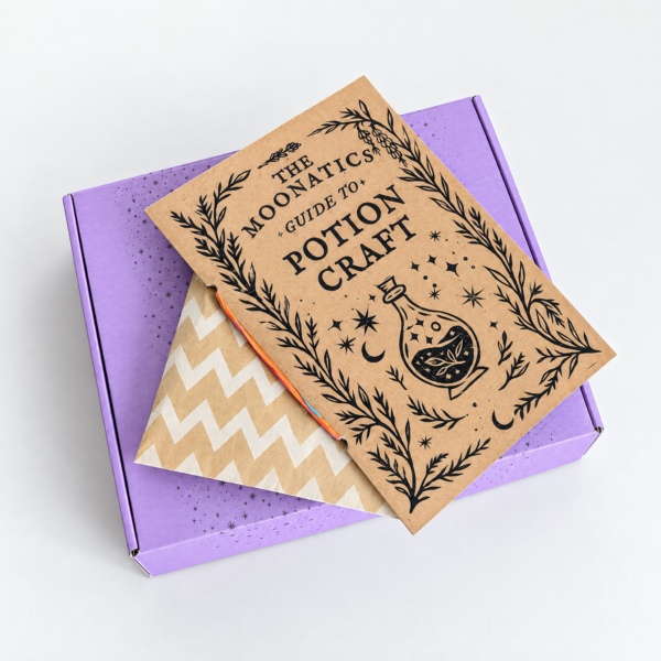 moonatics alchemist eco potion kit - closed box with booklet on top Purple Alchemist Eco Potion Kit gift box with illustrated Potion Craft guide and kraft envelope.