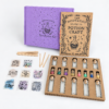 moonatics alchemist eco potion kit - full kit hero shot Complete Alchemist Eco Potion Kit with purple box, craft guide, glass bottles, mix-ins and wooden stirring sticks.